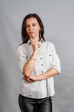 Beyaz gömlekli orta yaşlı ince kadın gri arka planda portre duruyor.