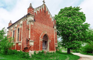 Ağaçların arkasında kırmızı tuğlalar olan terk edilmiş eski bir kilise. Çiçekli kestane