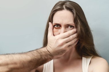 Erkek eli korkmuş bir kadının ağzını kapatıyor. Aile içi şiddet, adam kaçırma. Gözü morarmış olgun bir kadın ve yalıtılmış arka planda erkek eli var..