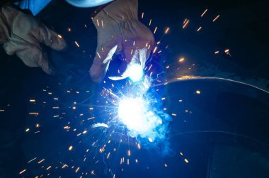 Parlak kıvılcımlarla kaynakçılığın mavi ışığı. Endüstriyel kaynak işlemi, iş yerindeki kaynakçı, karanlık arka planda. Metal kaynak fabrikası.