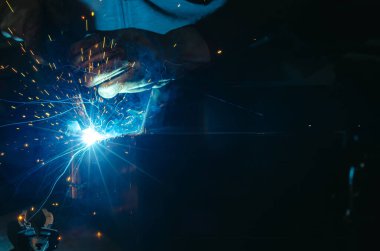 Parlak kıvılcımlarla kaynakçılığın mavi ışığı. Endüstriyel kaynak işlemi, iş yerindeki kaynakçı, karanlık arka planda. Metal kaynak fabrikası.