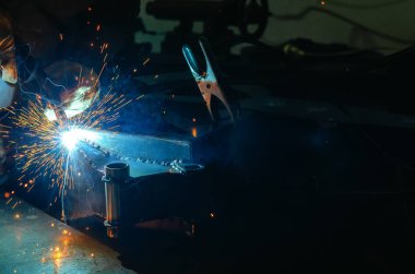 Parlak kıvılcımlarla kaynakçılığın mavi ışığı. Endüstriyel kaynak işlemi, iş yerindeki kaynakçı, karanlık arka planda. Metal kaynak fabrikası.