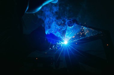 Parlak kıvılcımlarla kaynakçılığın mavi ışığı. Endüstriyel kaynak işlemi, iş yerindeki kaynakçı, karanlık arka planda. Metal kaynak fabrikası.