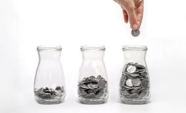 Farklı seviyelerde madeni paralarla dolu üç cam kavanoz, madeni para eklenmesi, mali büyüme ve tasarrufu simgeliyor.