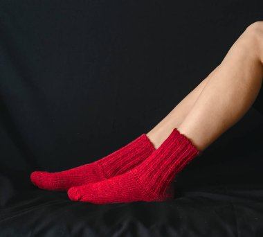 Siyah arka planda çıplak kadın bacaklarına sıcak kırmızı çorap örülmüş. Yan görüş. Sıcaklık, dinlenme ve rahatlık kavramı.