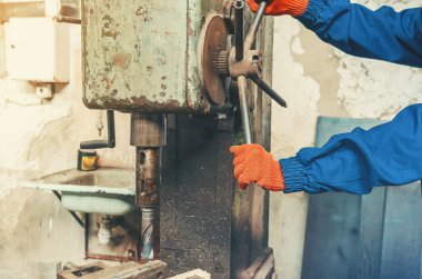 Mavi iş giysisi ve turuncu koruyucu eldiven giyen işçiler tarafından kontrol edilen endüstriyel sondaj işlemi. Hassasiyet, kontrol, endüstriyel güç ve profesyonel üretim becerileri kavramı.