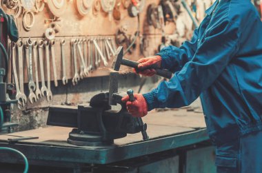 Mavi iş kıyafetleri ve turuncu koruyucu eldivenler giyen endüstriyel işçiler çekiç ve metal kelepçe kullanarak kıvılcım yaratıyor. Mekanik atölye..