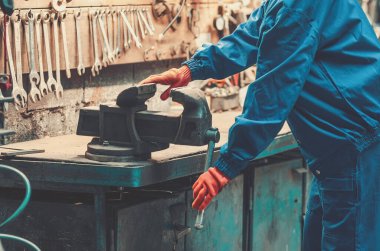 Mavi iş elbiseleri ve turuncu koruyucu eldivenleri olan endüstriyel işçiler metal kıskaç kullanıyor. Mekanik atölye.