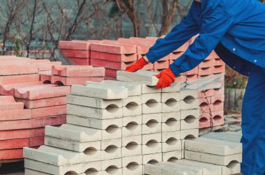 Koruyucu iş kıyafetlerindeki güçlü kadın işçiler, açık hava depolama alanındaki beton blokları dikkatle tutuyor ve istifliyor. Fiziksel çalışma kavramı, sanayide cinsiyet eşitliği ve modern işgücü kavramı.