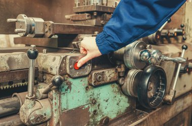 Fabrikada metal torna makinesi işleten mavi koruyucu üniformalı sanayi işçisi. Üretim süreci, ağır sanayi ve kalifiye işçilik kavramı.