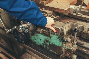 Fabrikada metal torna makinesi işleten mavi koruyucu üniformalı sanayi işçisi. Üretim süreci, ağır sanayi ve kalifiye işçilik kavramı.