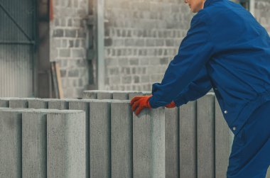 Fabrikanın içine beton ürünleri yerleştiren koruyucu giysiler giyen endüstriyel işçilerin yan görüntüsü. Kalite kontrolü, organize üretim, endüstriyel iş akışı.