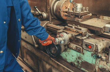 Üretim tesisinde mavi koruyucu üniformalı, metal torna makinesi kullanan endüstriyel işçilere yakından bakın. Üretim süreci, ağır sanayi ve kalifiye işçilik kavramı.