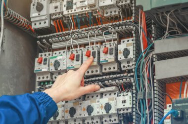 Elektrik kontrol paneli içindeki teknisyen el basma şalteri endüstriyel bakım, güvenlik prosedürleri ve güç yönetim sistemlerini vurguluyor..