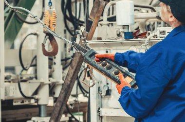 Mavi iş elbiseleri ve koruyucu eldivenleri olan profesyonel kadın sanayi işçisi fabrika bakımı sırasında ağır makineler kullanıyor. Endüstrideki kadın kavramı, eşitlik.