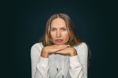 Beyaz elbiseli, uzun saçlı, elleri çenesinin altında, koyu arkaplanda kameraya bakan düşünceli bir kadının portresi. Psikoloji, akıl sağlığı, duygusal denge ve iç yansıma kavramı.