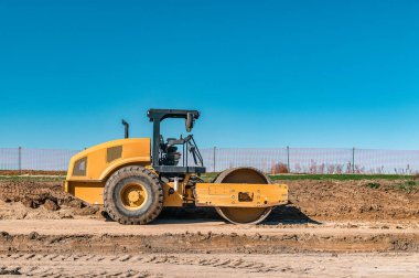 Açık mavi gökyüzü altında çalışan modern yol silindiri, büyük ölçekli inşaat ve altyapı geliştirme için hassasiyet, güven ve profesyonel sıkıştırma çözümlerini sembolize eder.