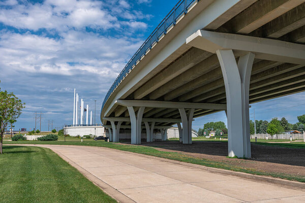 Coastal pedestrian area near bridge. Flags on white columns of bridge in Bismarck, USA. Blue sky with cumulus clouds background. Travel, tourism concept.