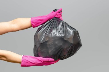 Gri stüdyo arka planında izole edilmiş pembe koruyucu eldivenlerle bağlanmış siyah çöp torbası. Temizlik ve günlük bakım konsepti. Boşluğu kopyala.