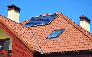 Energy efficiency concept. Close up of solar water panel heating on red tiled house roof with lightning protection, skylights, chimney and roof window clipart