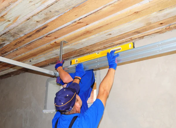 Contractors Installing Garage Door Metal Profil Post Rail and Spring Installation and Garage Ceiling. Spring Tension Lifts Section Garage Door Panel that Motor does not have to Lift Entire Weight.