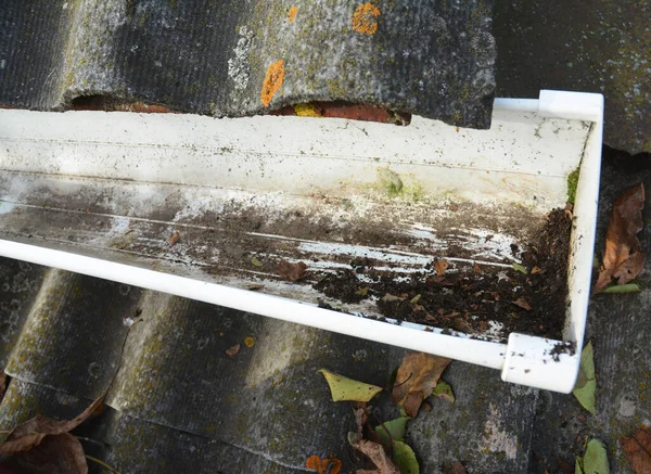 A rain gutter that has been blocked with dirt, debris and leaves is cleaned out to prevent damage to the roof and let the gutters collect rainwater freely.