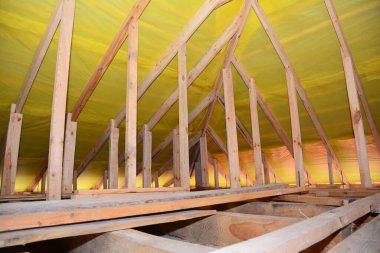 A view on unfinished attic from inside the house with a close-up on wooden ceiling joists, roof beams, rafters, wall studs and vapor barrier film installed under the roof.  clipart