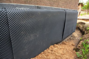Installation of waterproofing dimpled membrane to insulate exterior basement or foundation wall of a brick house against moisture and water leakages. clipart