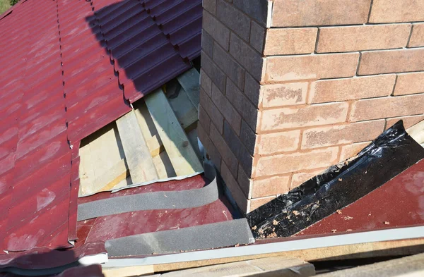 A close-up on a roofing construction, installation of metal roof tiles on wood roof sheathing around a brick chimney using waterproofing corner flashing.  Roofing construction.