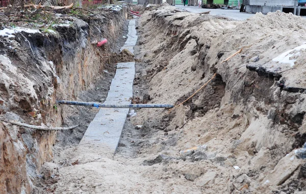 An excavated trench with underground cables, electricity and telecommunication lines installed and covered by protective concrete slabs in a new residential areas. Cable damages during excavation.