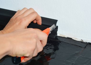 Becerikli bir adam siyah plastik bir etek tahtasını beyaz bir duvara yerleştiriyor ve bir alet bıçağıyla kesiyor.. 