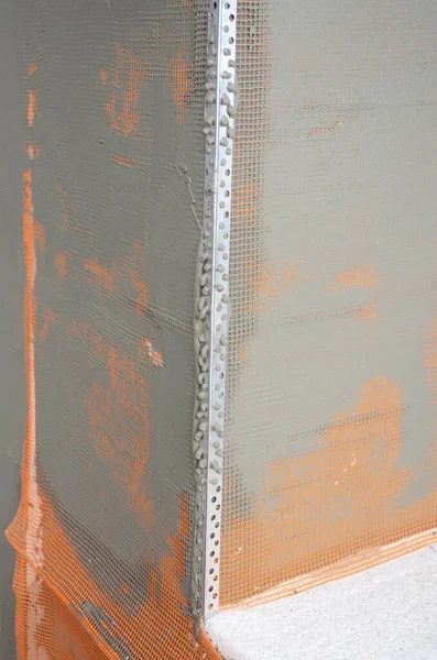 A close-up on a rendered, plastered corner with fiberglass mesh and angle bead applied around the window area while installing external wall insulation.