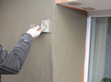 Bir DIyer, ev sahibi veya profesyonel, dış duvar yalıtım sürecinde spatula kullanarak pencere alanı içinde son render kaplama uyguluyor. 