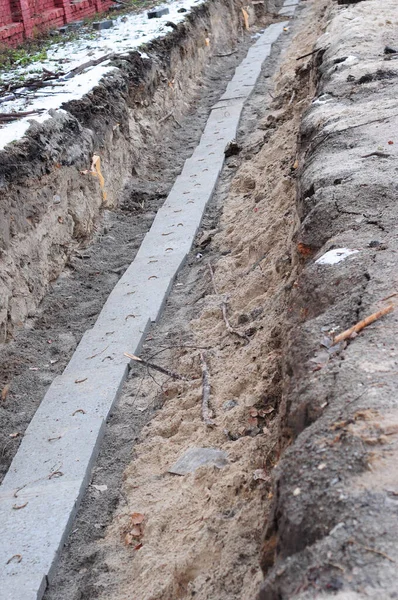 A close-up of a cable trench excavation with underground cables installed and covered with protective concrete slabs to provide electricity and telecommunications to new residential districts. — Stock Image Close Cable Trench Excavation Underground Cables Installed Covered Protective Concrete Royalty Free Stock Photos