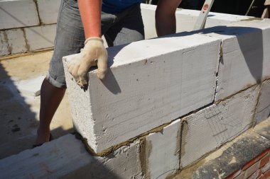 Bir inşaat müteahhidi, ziftli asfalt su yalıtımı zarı döşenmiş tuğla temelin üzerine otoklakaplı beton (AAC) bloklar inşa ediyor..