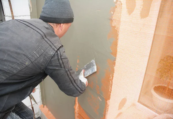 一个杂工在大楼外墙的窗区周围的玻璃纤维增强网罩上剥皮 粉刷外墙 并涂水泥 — 图库照片