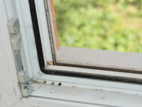 A close-up on an opened upvc / pvc window frame with rubber seal, lock rollers and mosquito screen installed and dirty window tracks covered in dust that need cleaning.