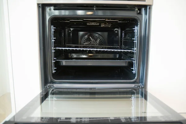 Choosing kitchen appliances, electric oven: An inside view of an electric built-in stainless steel oven, stove of fan oven type with shelves and racks.