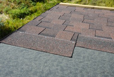 Installing brown dimensional asphalt roof shingles on the underlayment, water-resistant, waterproof protection barrier material on the rooftop of the house construction during house repairing. clipart