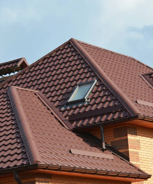 A close-up of a metal roofing waterproofing problem area with roof flashings, a complex roof with valleys, a skylight window, snow guards or snow stoppers.