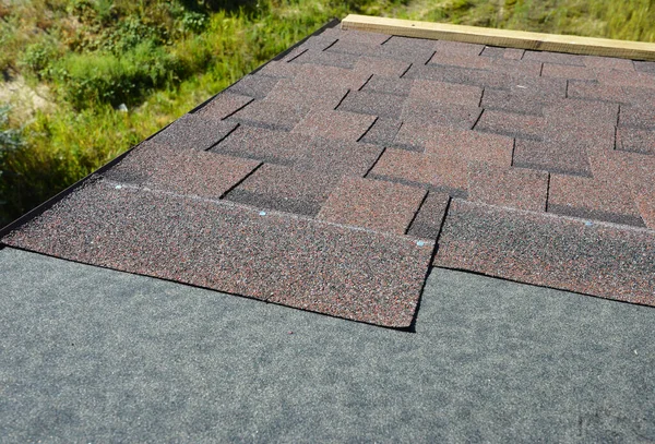 Installing brown dimensional asphalt roof shingles on the underlayment, water-resistant, waterproof protection barrier material on the rooftop of the house construction during house repairing.