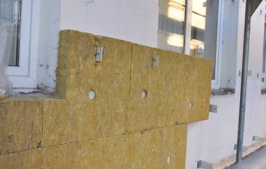 High performance external mineral wool insulation: A close-up of mineral wool batts, boards installation with broad cap anchors on the outside wall of the house.  