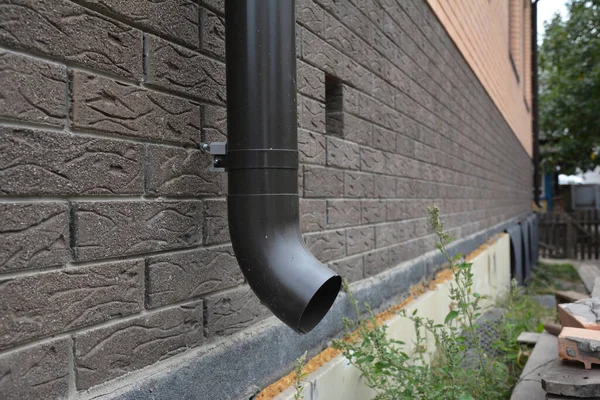 A close-up on a metal rain gutter downpipe, downspout of a roof gutter system and a foundation vent of a new house.