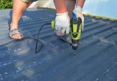 Çatı inşaatı: bir çatı müteahhiti metal çatı levhaları yerleştiriyor, metal çatı kiremitleri elektrikli tornavidayla vidaları sürüyor.