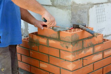 Masonluk tuğla işi. Müteahhitlerden biri evin köşesinde duvar örüyor. Duvarları beton blokla örüyor. Kürek, havan topu ve çekiçle onları birbirine bağlıyor..
