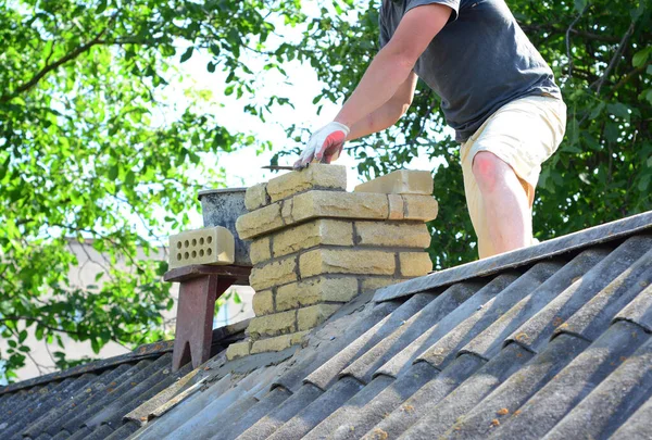 Chimney construction and re-building. A contractor is building a chimney on an asbestos roof.