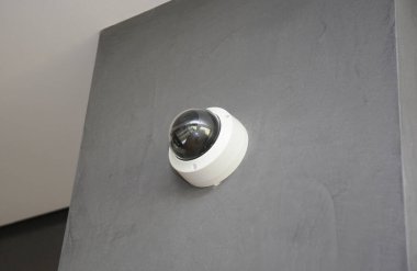 Yuvarlak bir güvenlik kamerası, modern bir apartmanın içinde gri bir duvara yerleştirilmiş güvenlik kamerası..