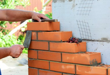 Tuğla ve beton blok duvar inşaatı. Bir duvar ustası beton blok bir duvara tuğla örüyor. Kürek, çekiç ve örgü duvar teli kullanıyor..