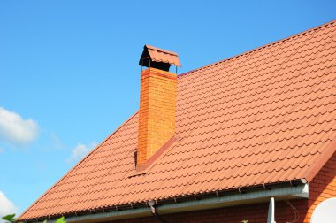 Soluk kırmızı metal kiremit, yağmur oluk ve baca mavi gökyüzü karşı.