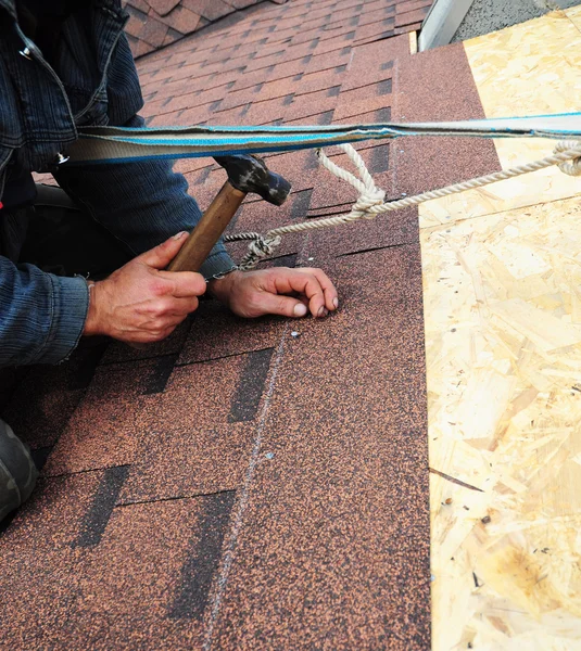 Roofer installs bitumen roof shingles with hammer and nails - cl — Stock Photo, Image